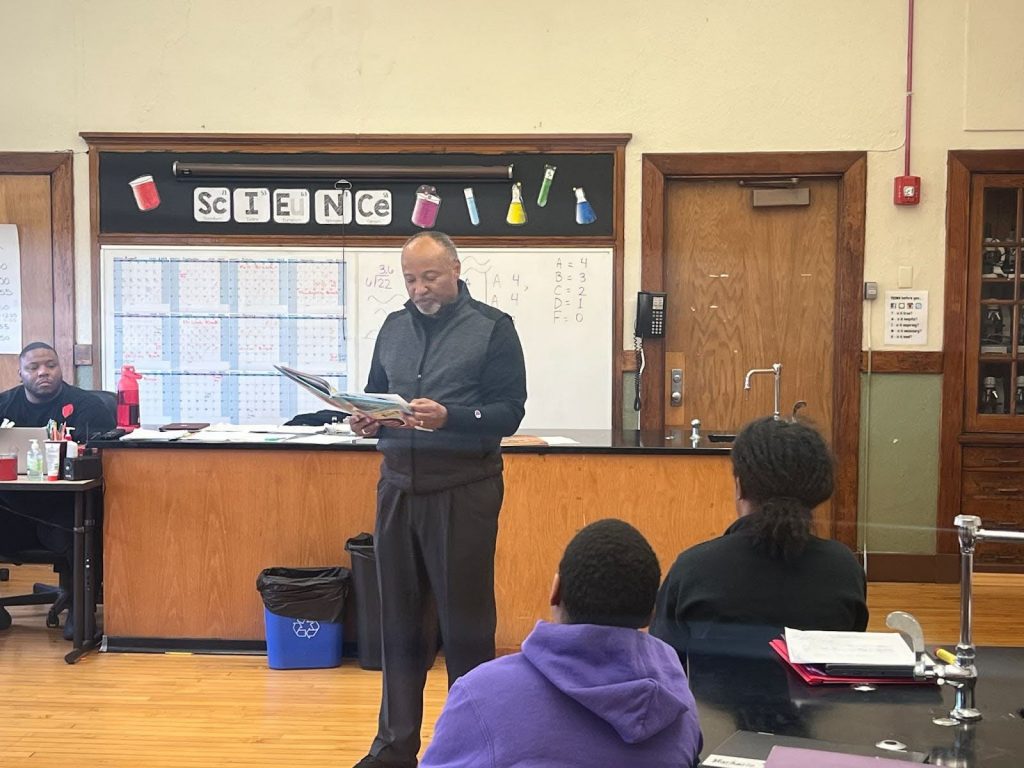 man reads a book at the front of a classroom