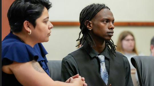 Melina Hettiaratchi and Jonah Bevin sit together in a court room, their attention on someone else out of sight.