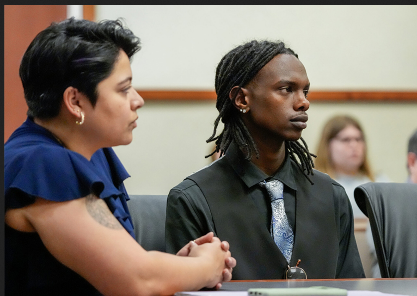 Melina Hettiaratchi and Jonah Bevin sit together in a court room, their attention on someone else out of sight.