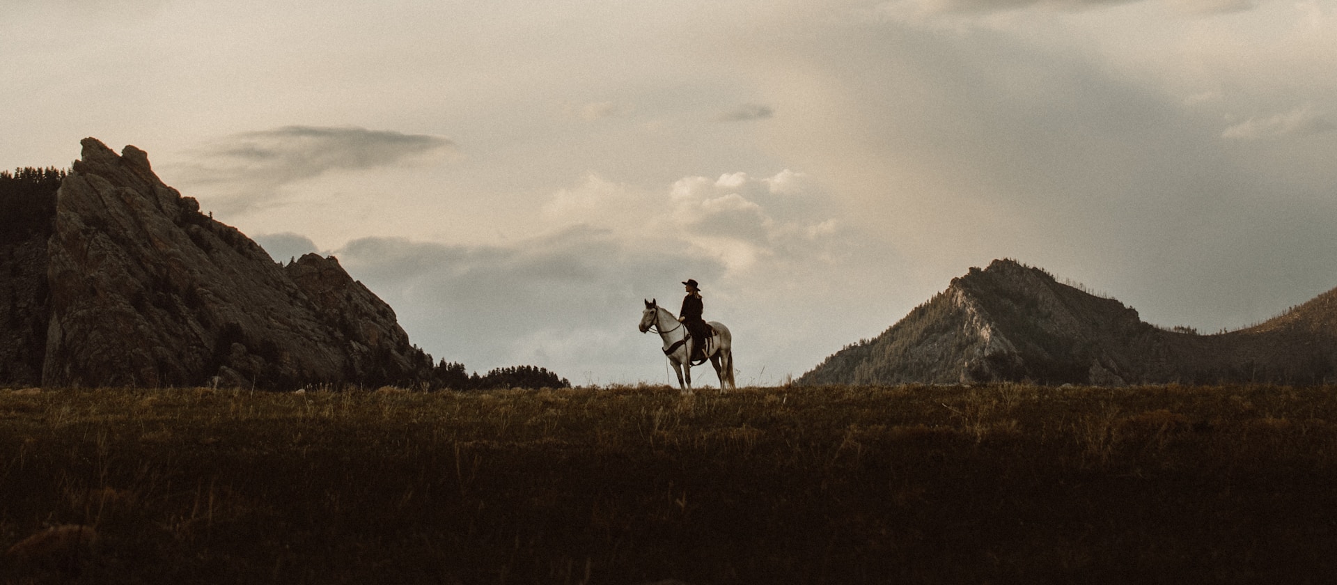 A lone horse rider against stands on a field with two mountains in the background.