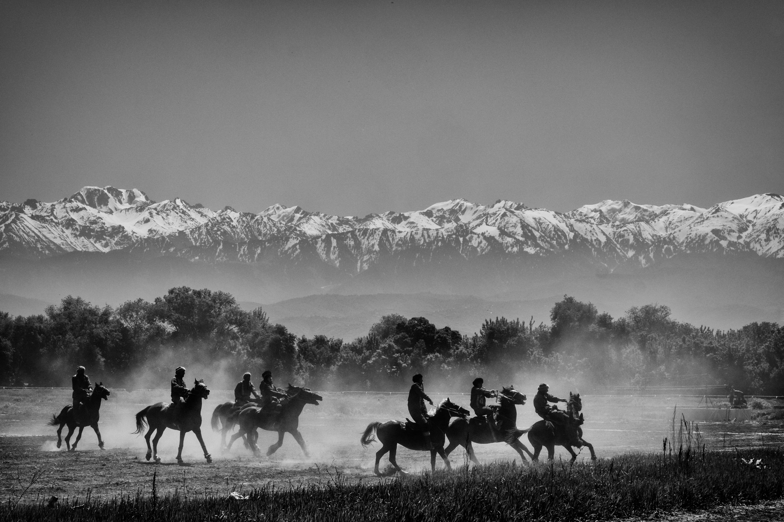 A black and white photo of a group of people riding horses. In the background, a mountain range is visible through fog.
